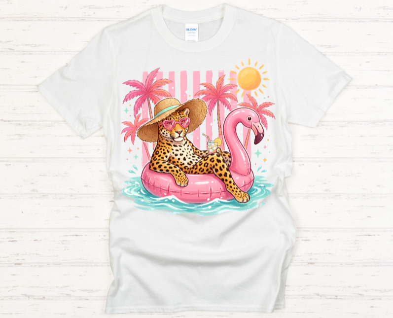 White t-shirt with a colorful graphic of a leopard on a pink flamingo float with palm trees and a sun in the background.