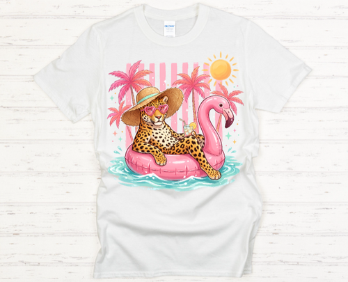 White t-shirt with a colorful graphic of a leopard on a pink flamingo float with palm trees and a sun in the background.