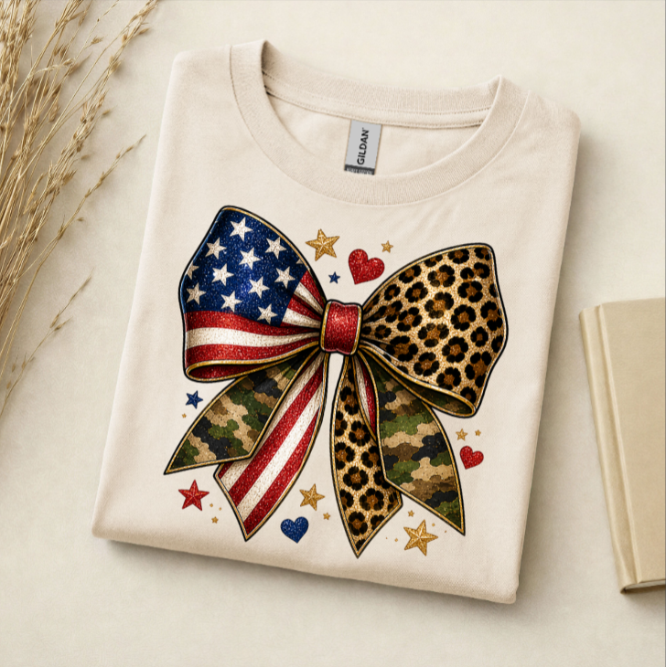 White t-shirt with a colorful bow design featuring American flag, leopard print, and camouflage patterns